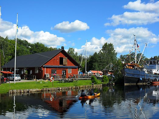 En kanot i Hjälmare kanal med röd byggnad i bakgrunden.