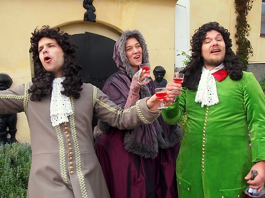 Tre skådespelare med glas i hand och klädda i medeltida kläder.